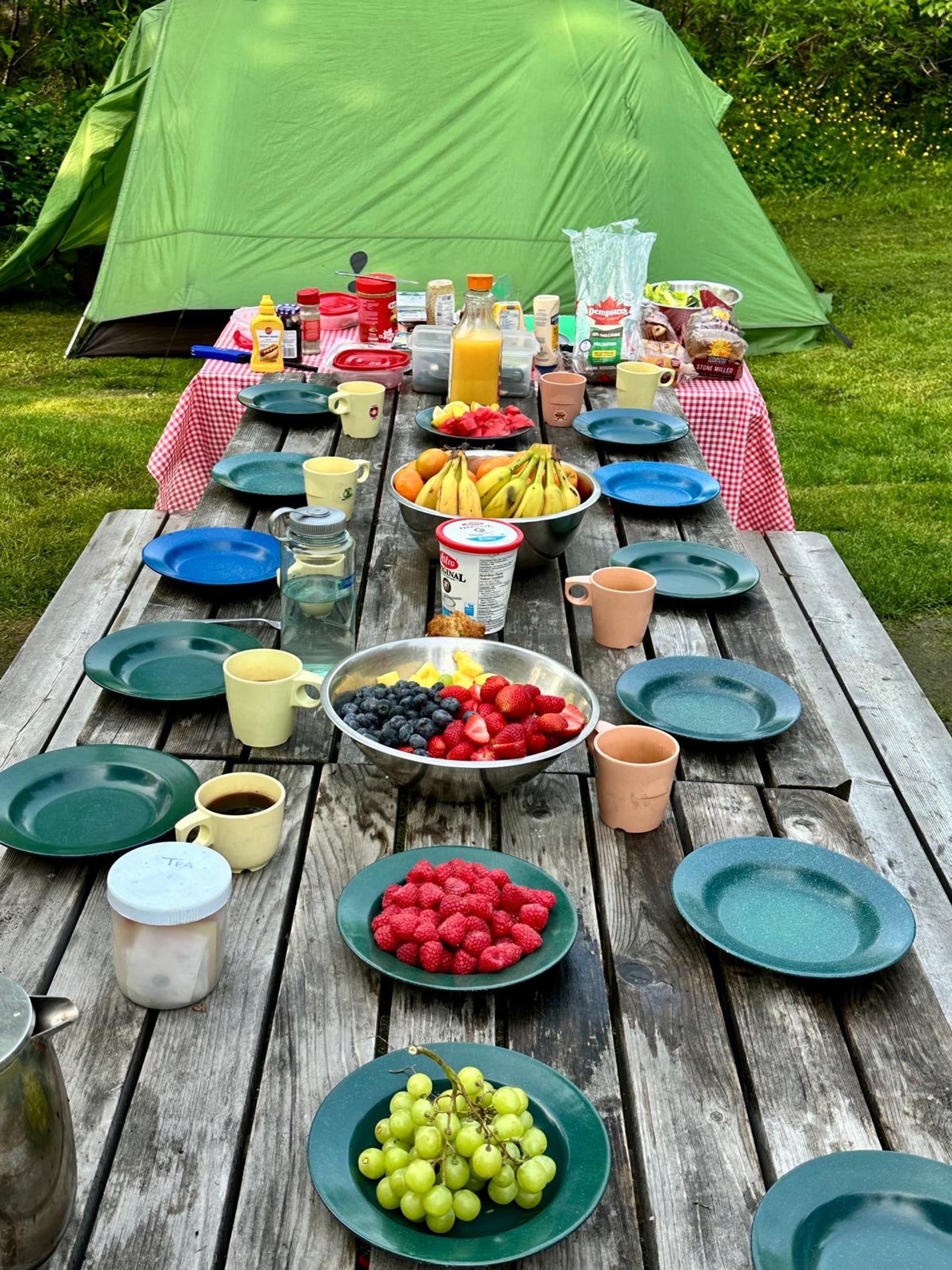 Picnic table full with breakfast foods with tent behind. 