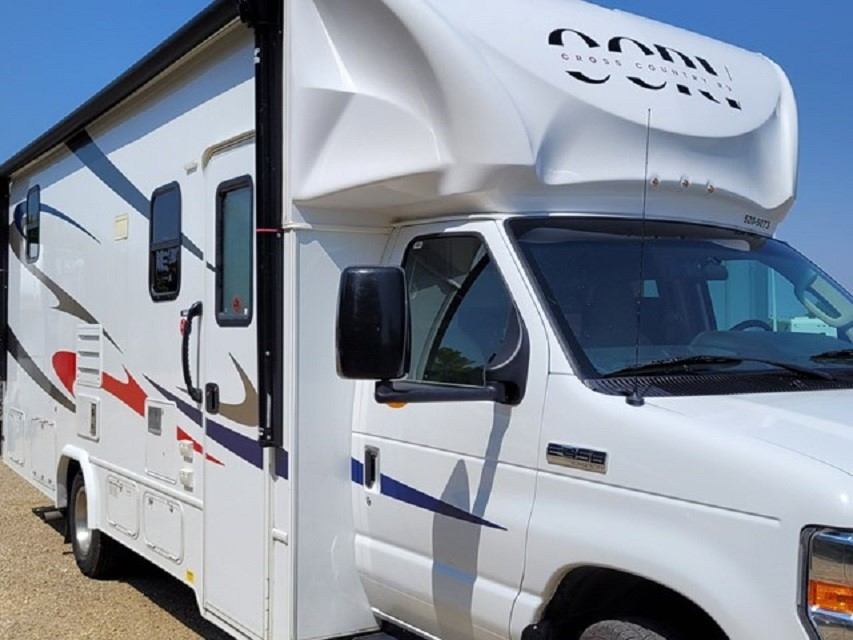 White RV parked beside a blue road sign, showing a slide-out and front cabin.