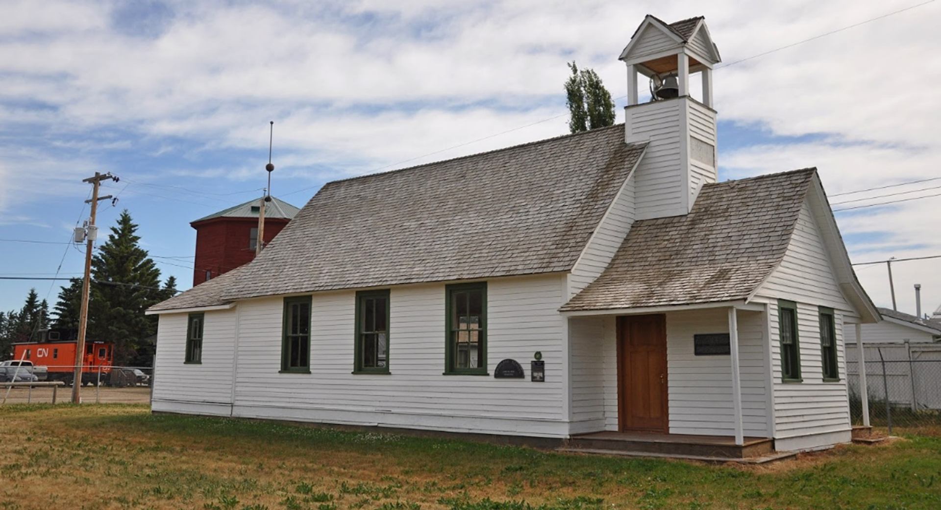 White wooden church with bell tower, green-trimmed windows and shingled roof.