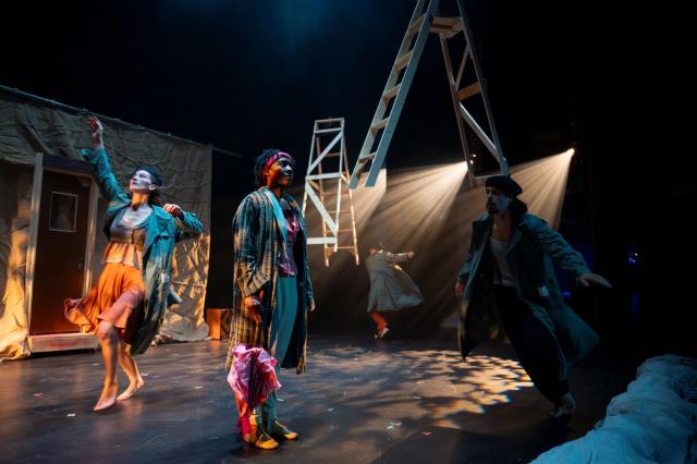 Four costumed performers on stage and two wooden ladders suspended in the air, all lit by dramatic theatrical lighting.