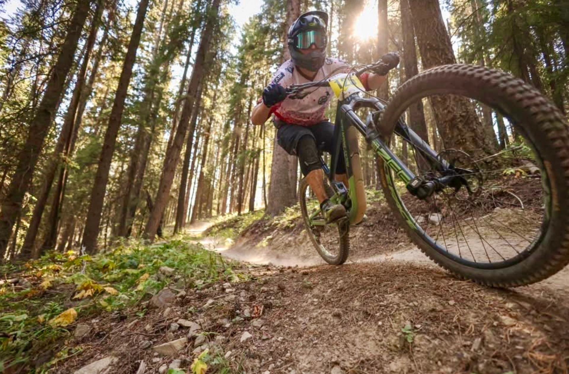 Mountain biker rides a trail through a forest, handlebars and front wheel visible.