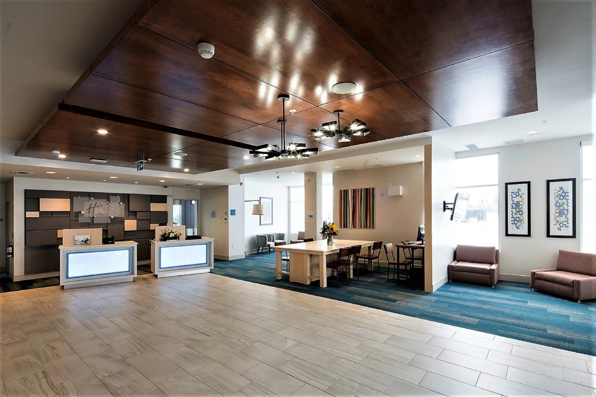 Modern hotel lobby with sleek wooden ceiling, contemporary chandeliers, and a spacious seating area. The reception desk is minimalist, creating an inviting atmosphere.