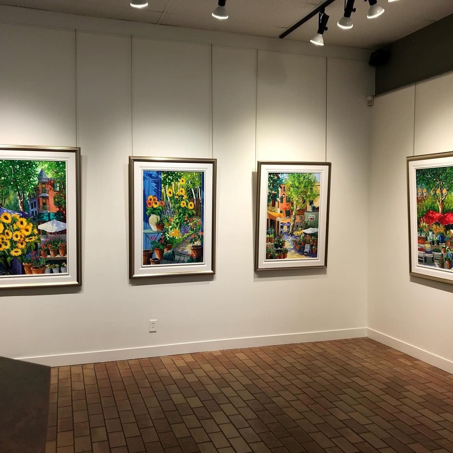 Art gallery wall with framed paintings, white display panels and ceiling track lights.