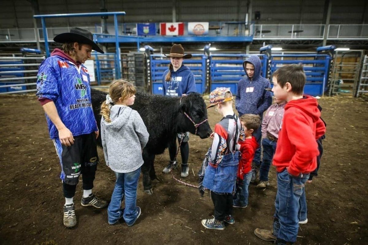 Children and adults in western clothing stand around a small black calf inside an arena.