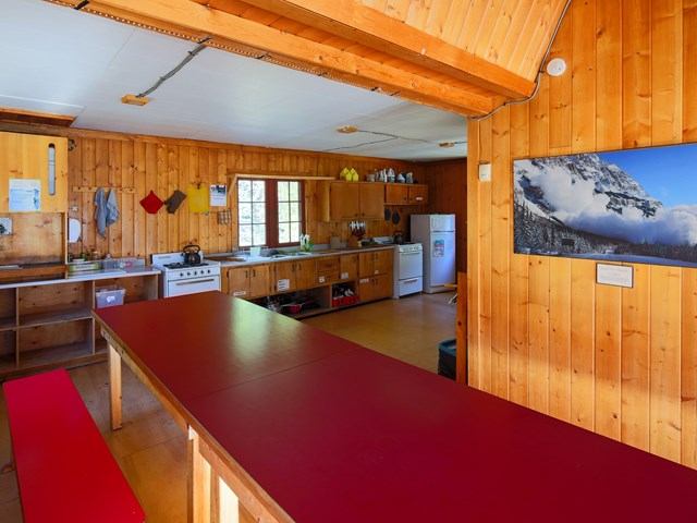 Rustic kitchen with red table, wood walls, and mountain photo in a cozy cabin setting.