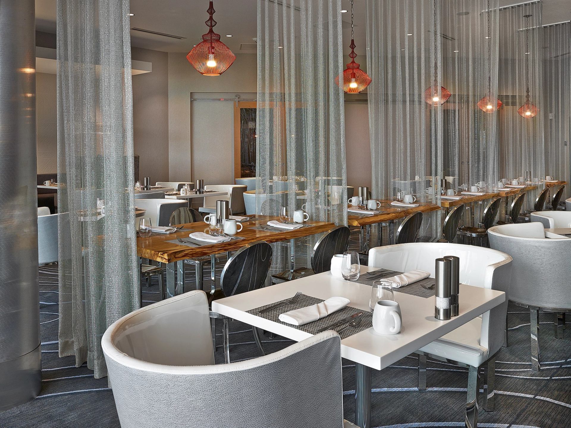 Elegant dining area with sheer curtains, red pendant lights, and white table settings.