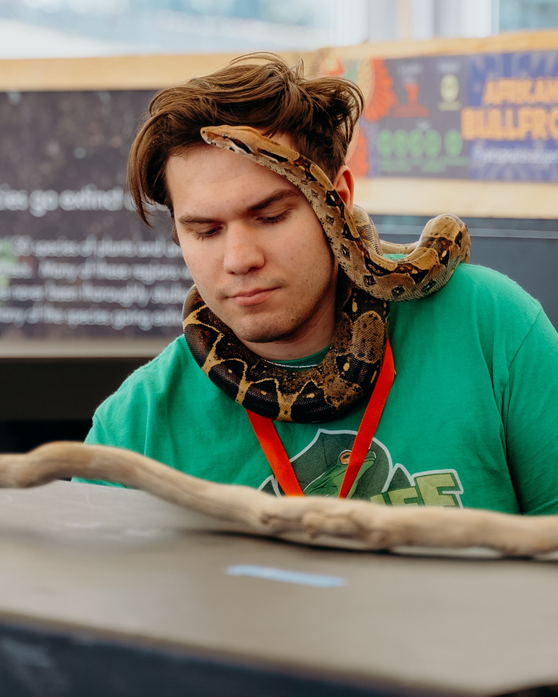 A person with a snake resting around their shoulders at an animal display booth.