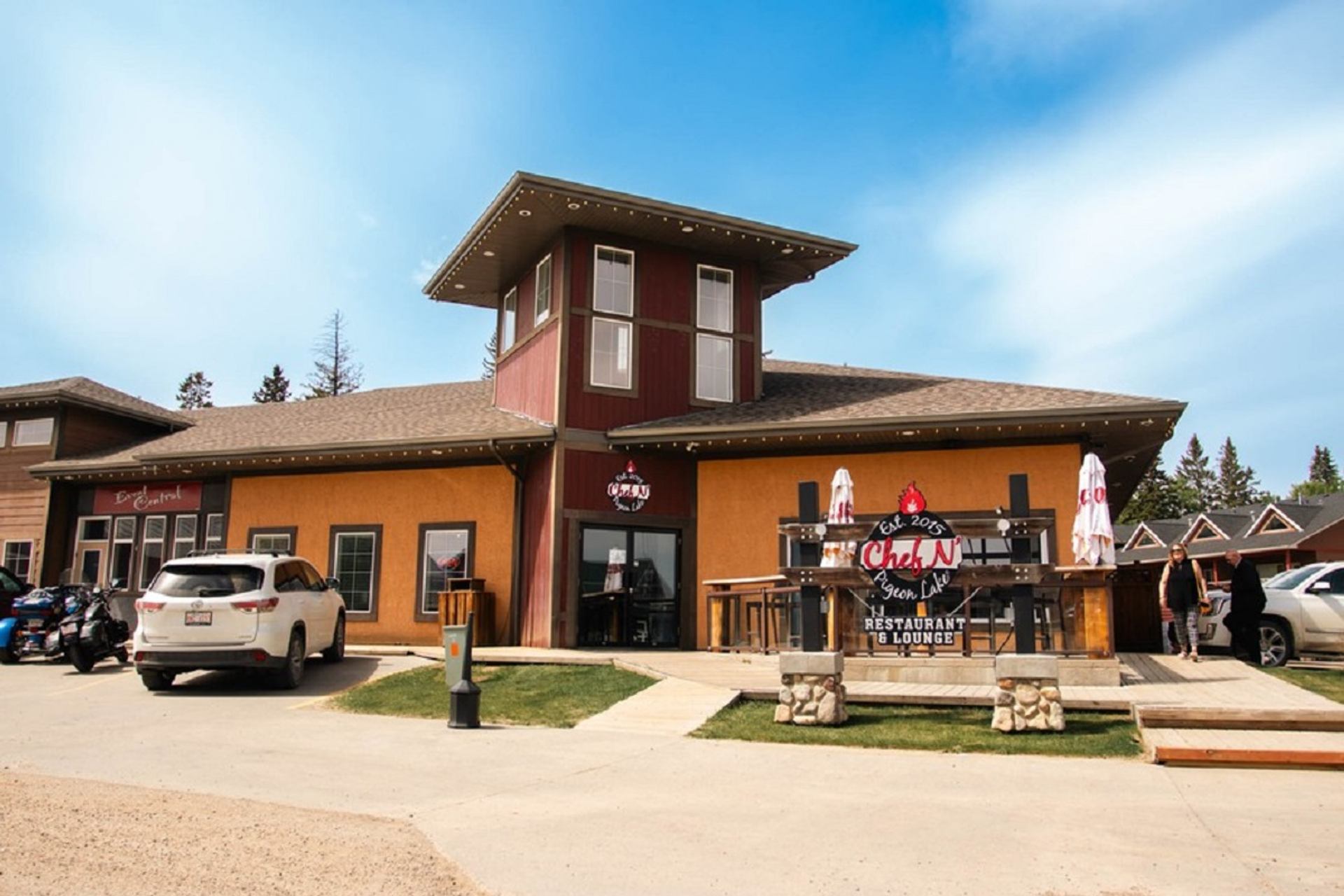 Chef N’ Pigeon Lake with outdoor seating and parked cars under blue sky.