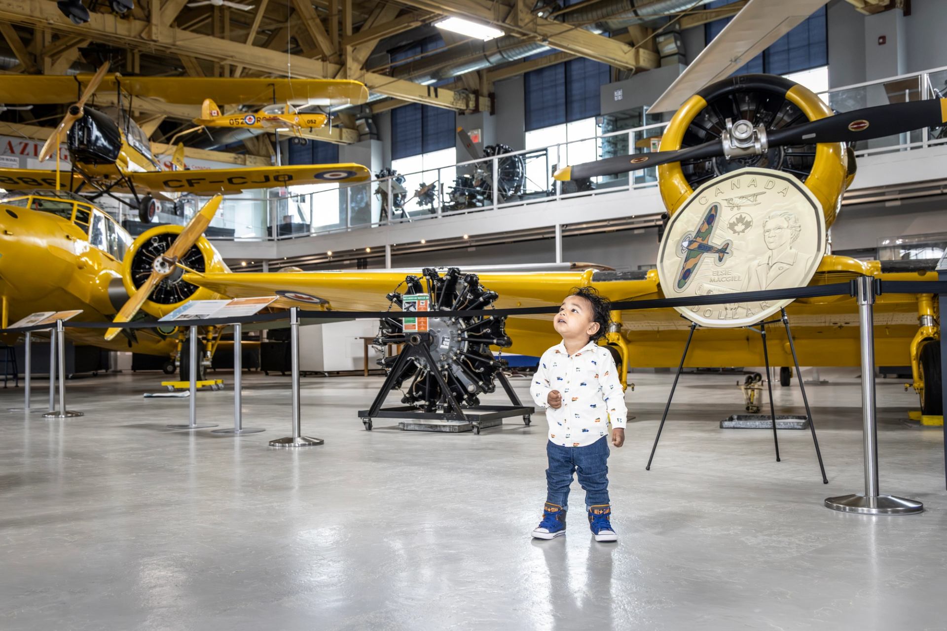 Child looks up at yellow aircraft displayed inside an aviation museum.