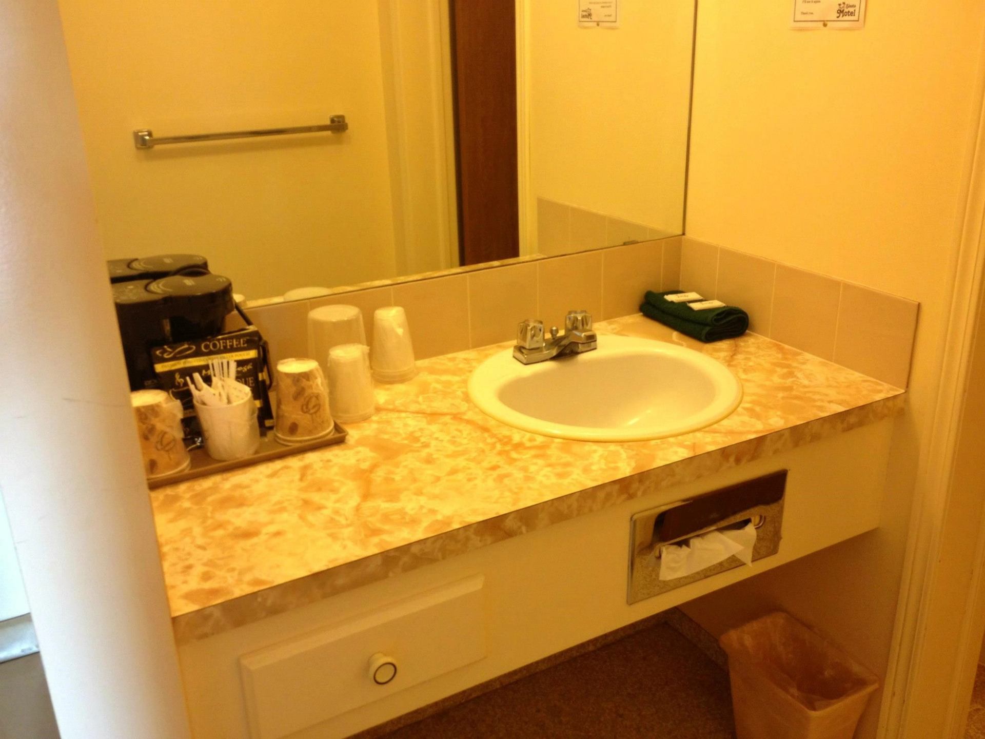 Motel vanity with marbled counter, sink, mirror, and toiletries.