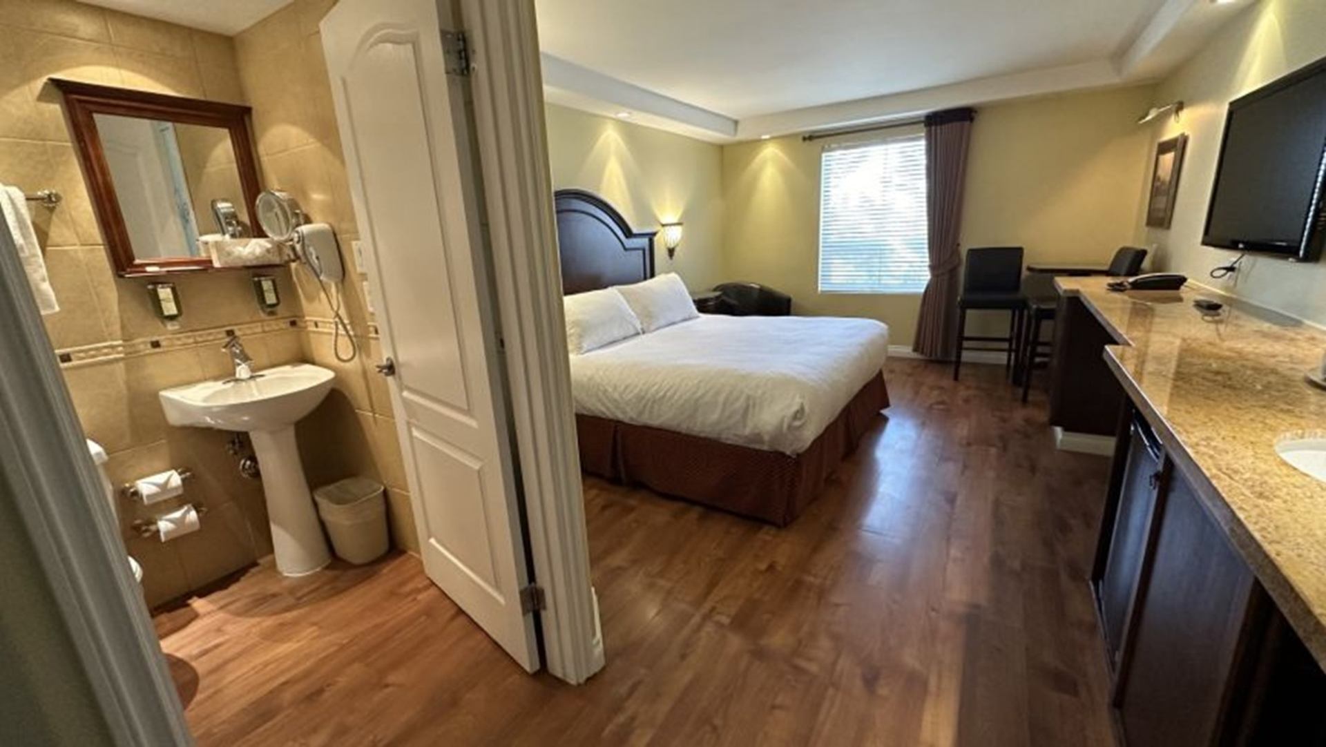 Hotel room with bed, open bathroom door, hardwood floor, desk, chairs and television.