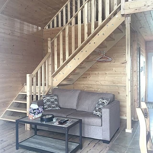 Rustic living area with a gray sofa, wooden coffee table, and staircase leading to a loft.