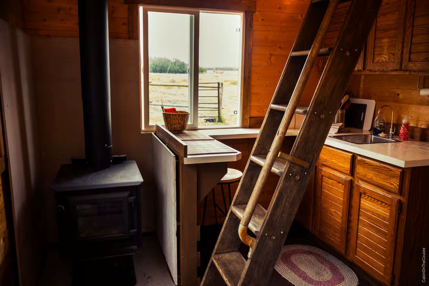Interior with a wood stove, window bar seating, and wooden kitchen cabinets.