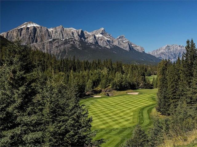 Golf course with striped fairway and rocky peaks in background