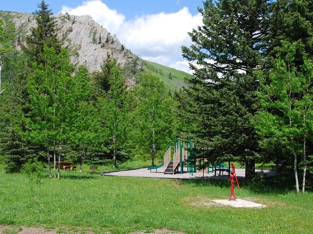 Playground set in a grassy clearing surrounded by trees and rocky hills