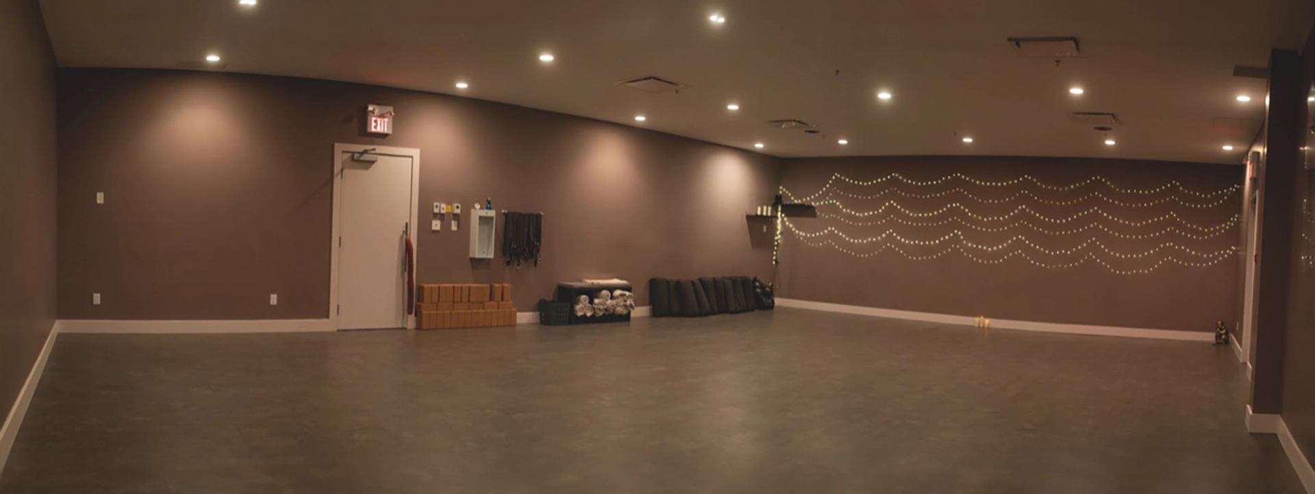 Spacious yoga room with mats, string lights, and soft lighting.
