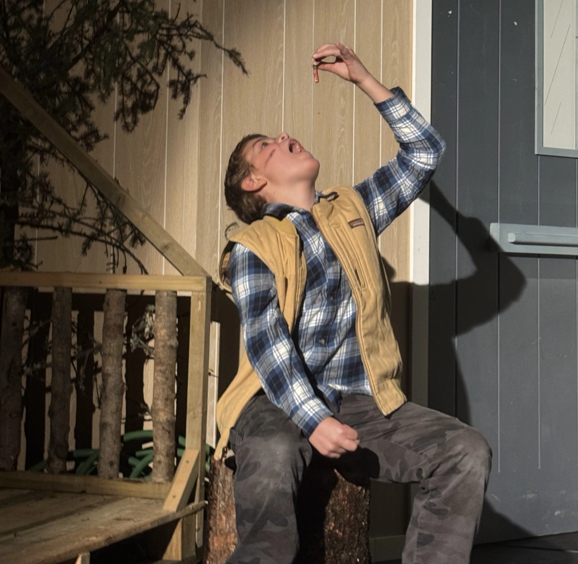 Person in plaid shirt outdoors, holding something above mouth.