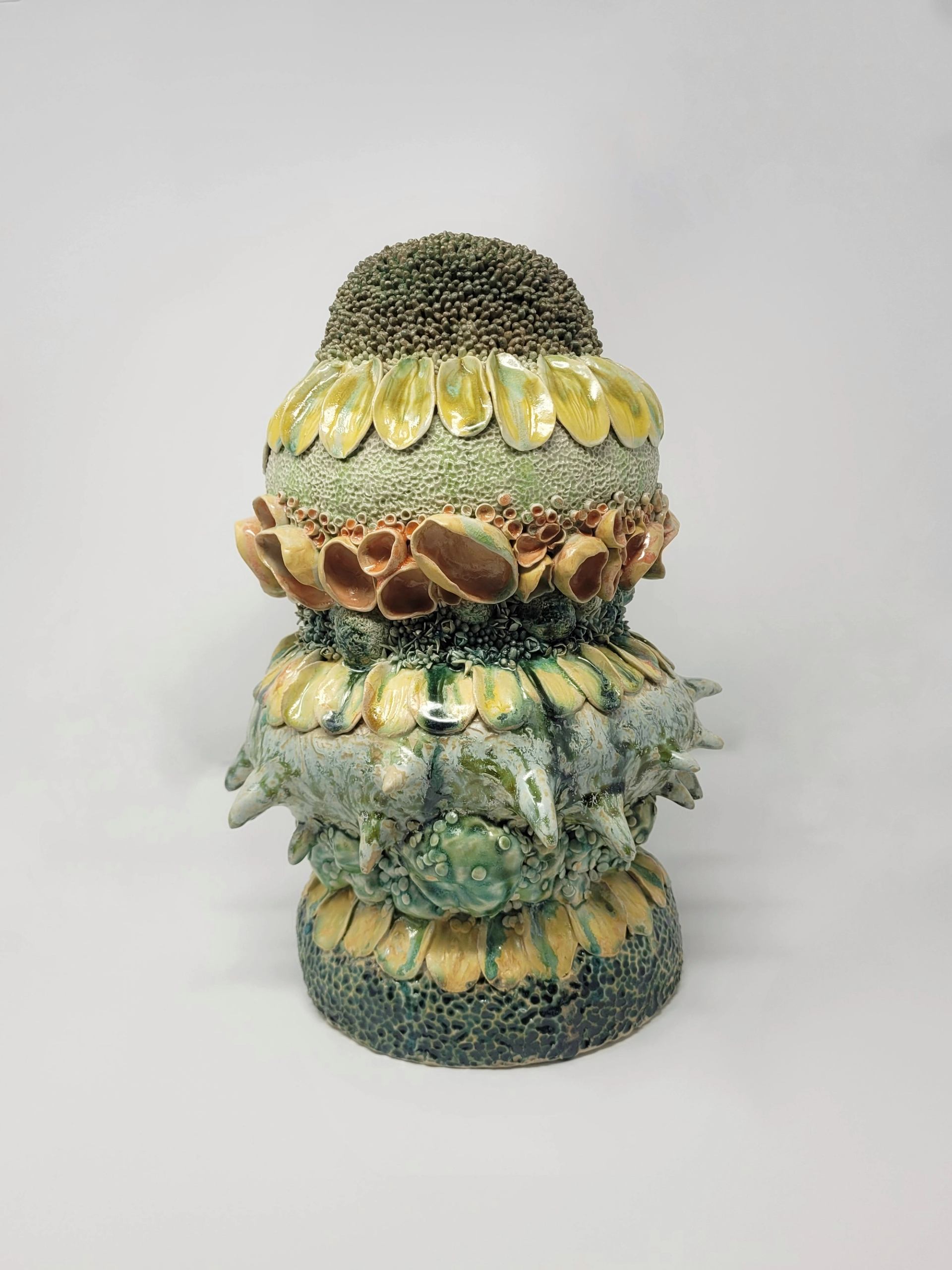 Textured ceramic sculpture with layered organic shapes and yellow-green glazes on white background.