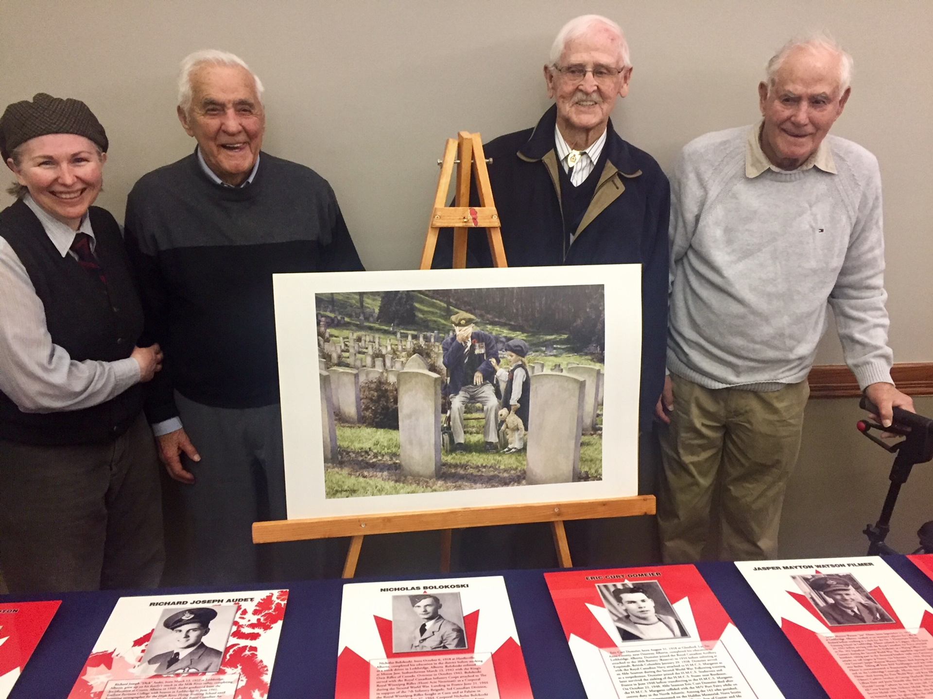 Four people stand behind easel photo of cemetery, above display of veteran biographies.