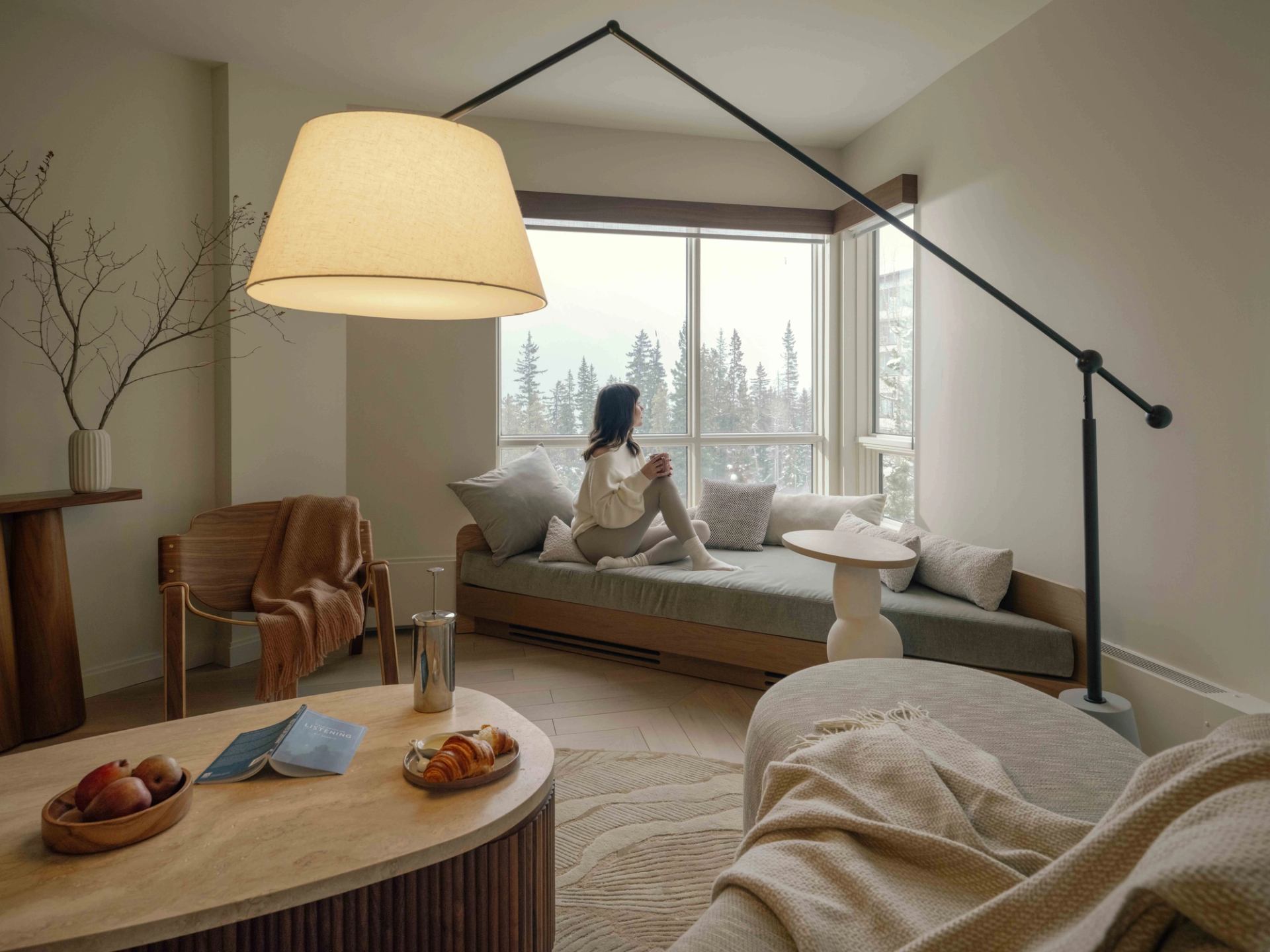 Hotel sitting area with a window bench, pillows, modern lighting, and forest views at Rimrock Banff.