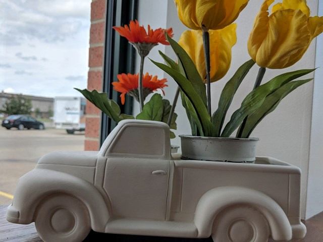 Ceramic pickup truck planter holding orange and yellow flowers on windowsill.