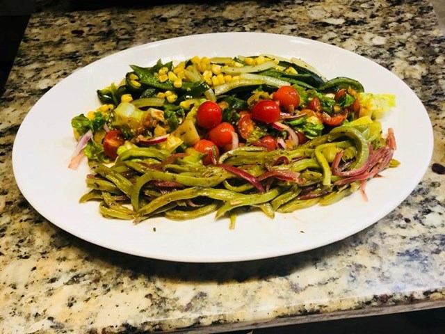 Colorful Mexican salad with cactus, cherry tomatoes, corn, and onions on a white plate.