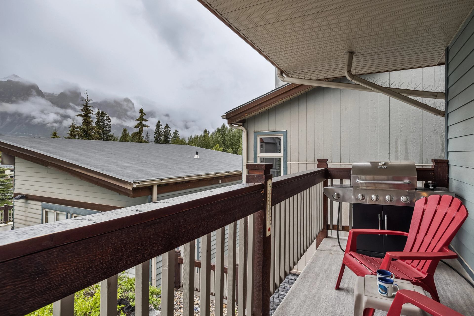 Covered balcony with red chairs, barbecue and misty mountain view.