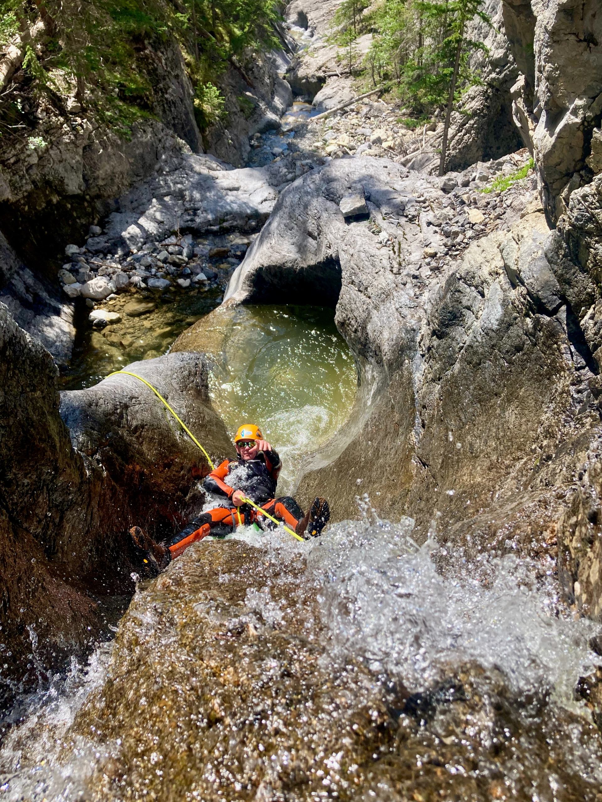 Canyoner rappelling down a steep waterfall into a rocky pool in Bow Valley.