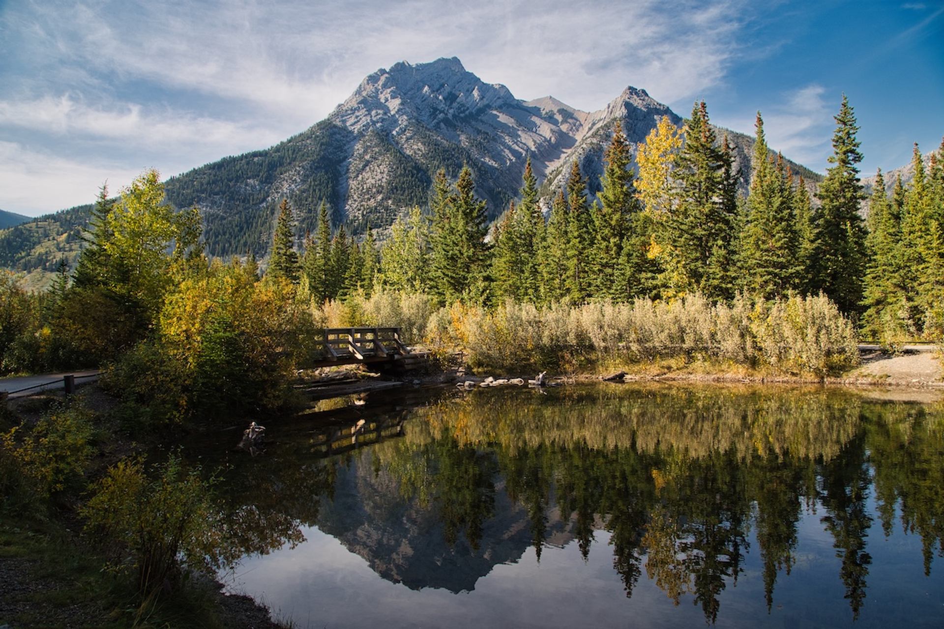 Pond reflecting trees and a rocky mountain peak at Mt. Lorette Ponds. 