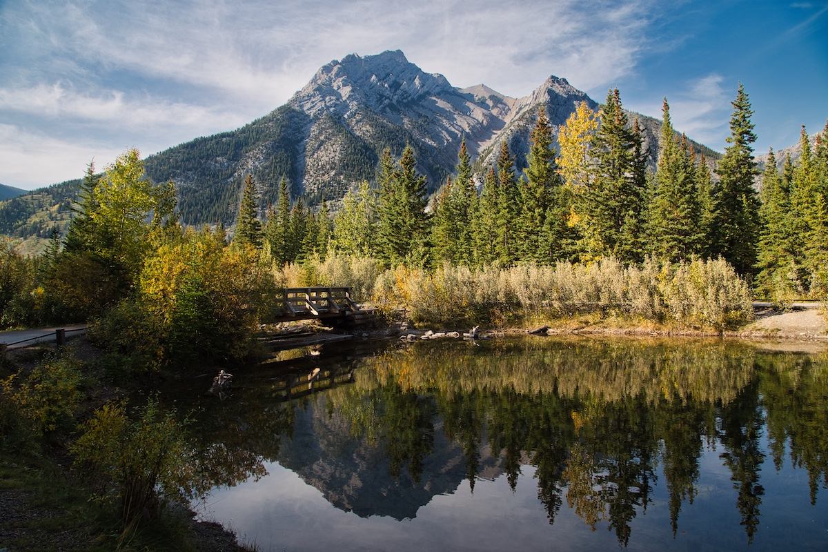 Pond reflecting trees and a rocky mountain peak at Mt. Lorette Ponds.