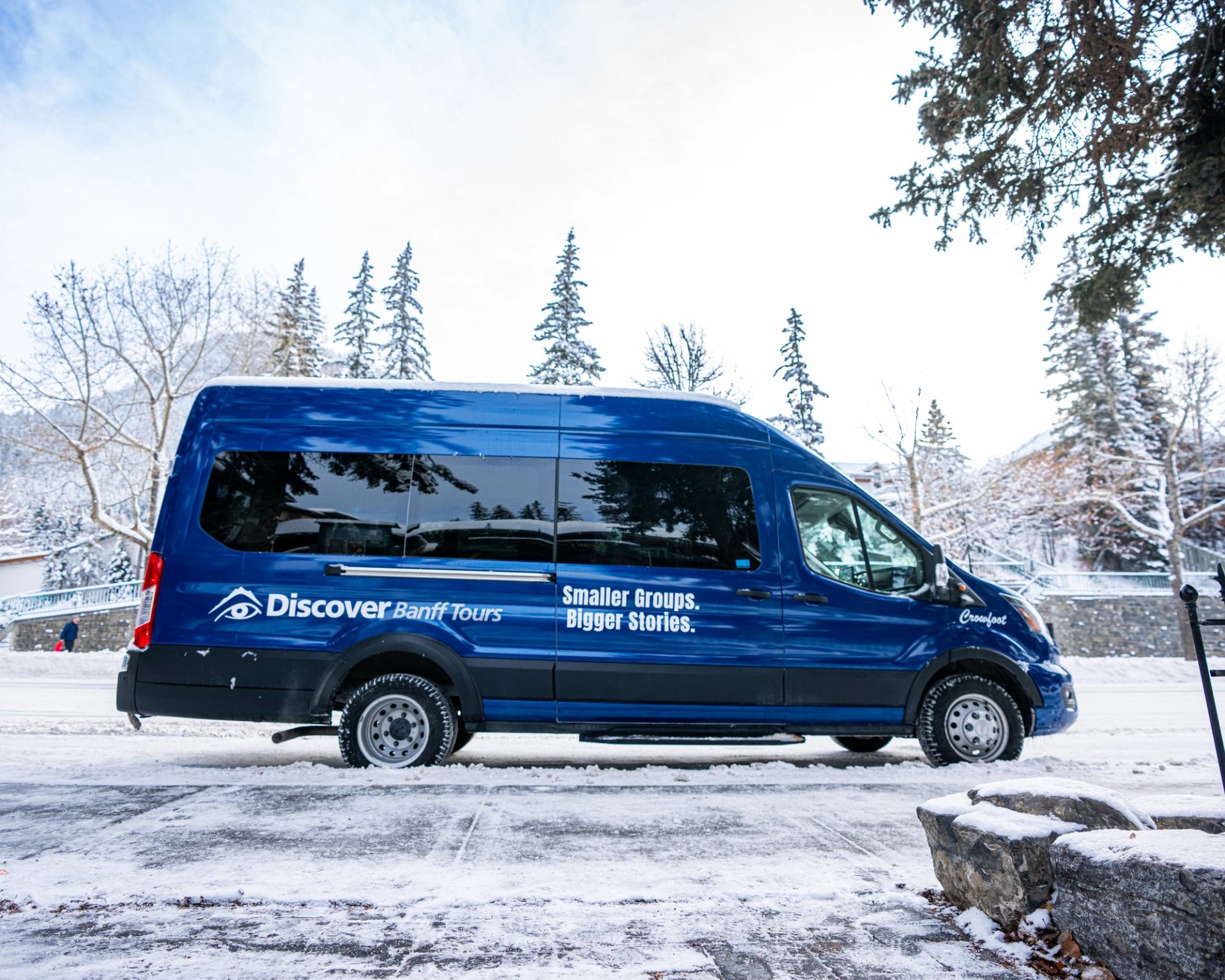 Blue Discover Banff Tours van parked on snowy street with snow-covered trees.