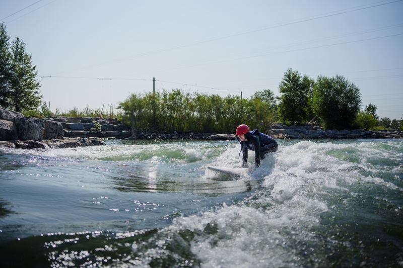 A river surfer on the Harvie Passage wave getting up on a surfboard.