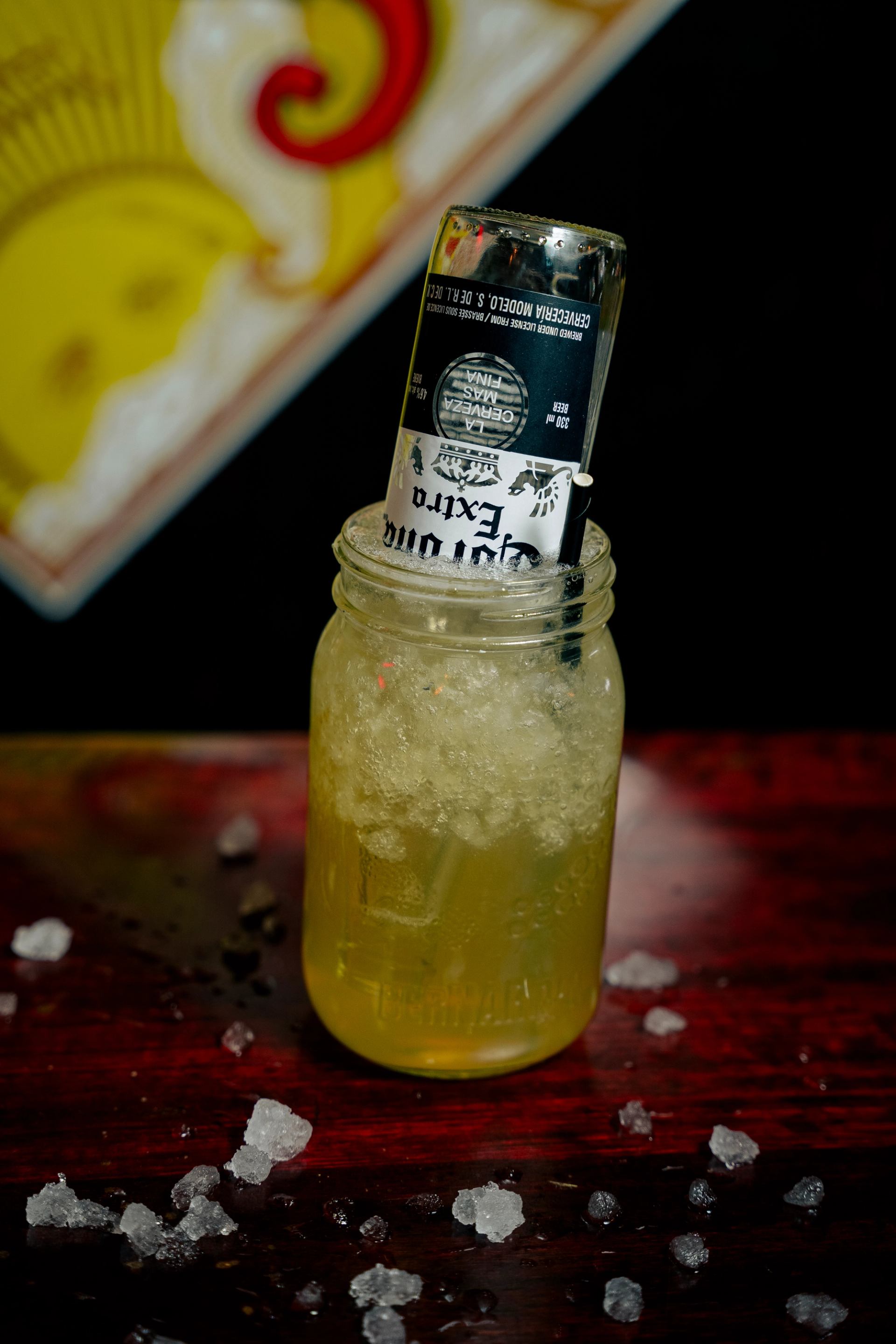 Glass jar cocktail with lime-green drink, black label, and ice on wooden table.