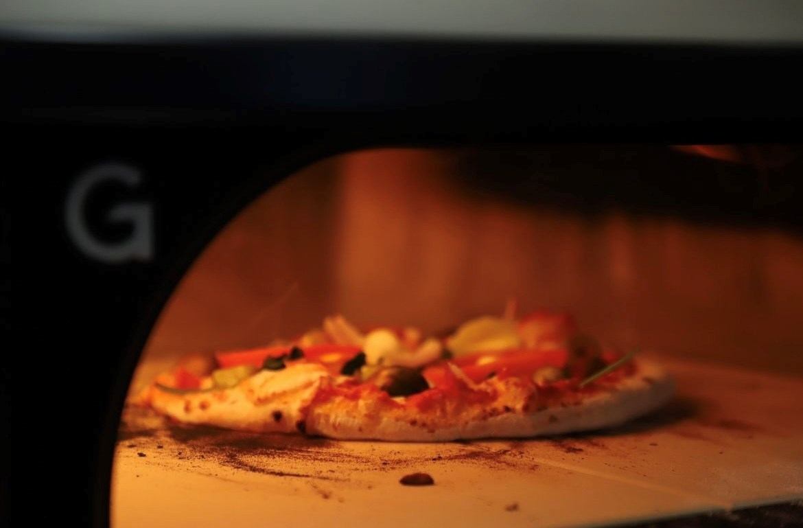 Pizza on an indoor table with toppings and cheese under warm lighting.