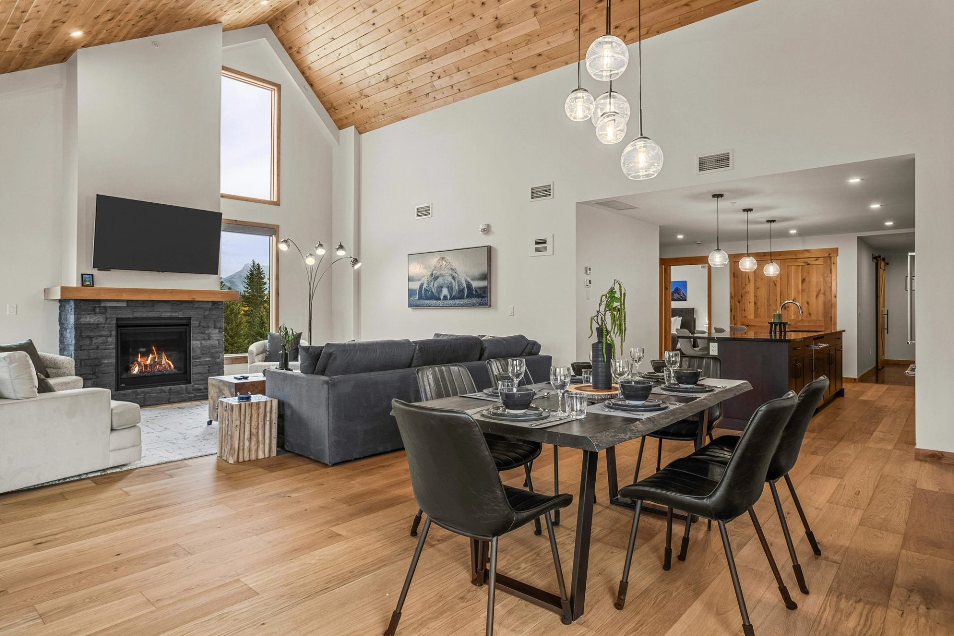 Open-concept dining and living room with vaulted wood ceiling, fireplace and kitchen.