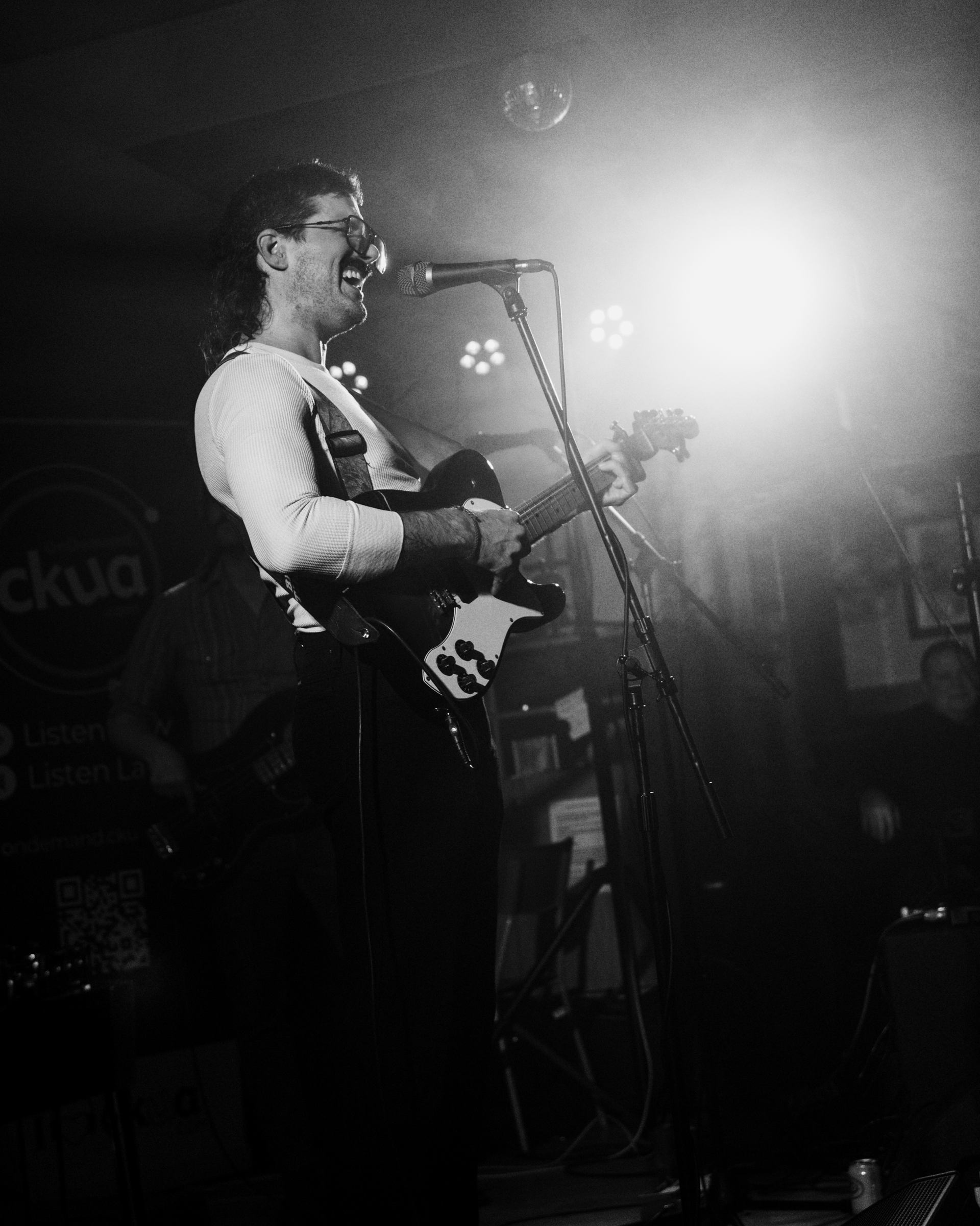 Musician playing electric guitar under bright stage lights in a black-and-white photo