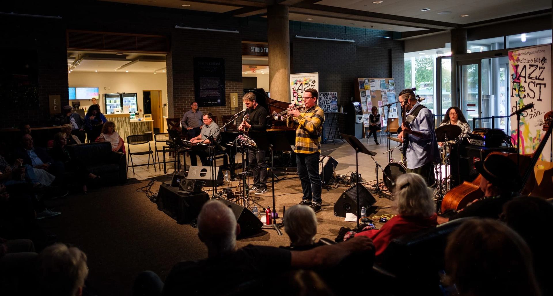 Jazz band performs on indoor stage as seated audience watches in dimly lit venue.
