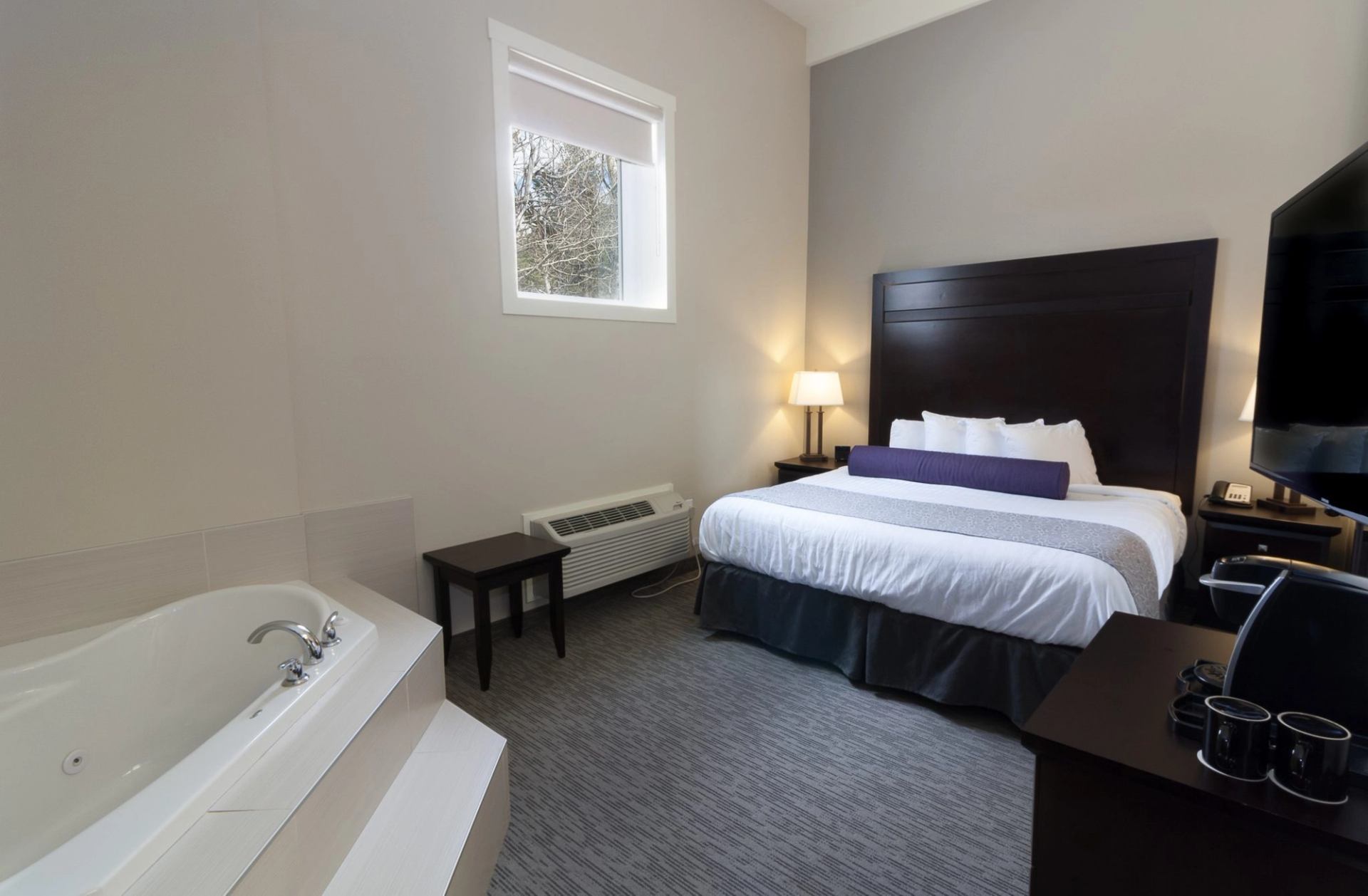 Hotel room with a bed, whirlpool tub, television, window and coffee station.