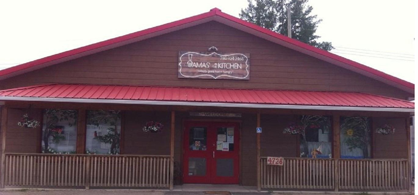 Restaurant storefront with “Mamas’ In The Kitchen” sign, red doors, and porch railing.