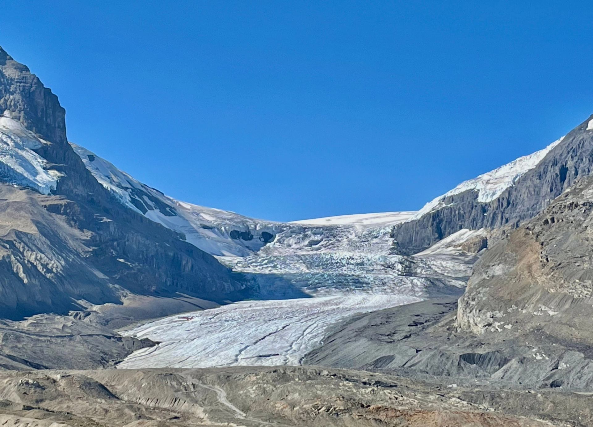 Glacier flowing between rocky mountain slopes under a clear blue sky.
