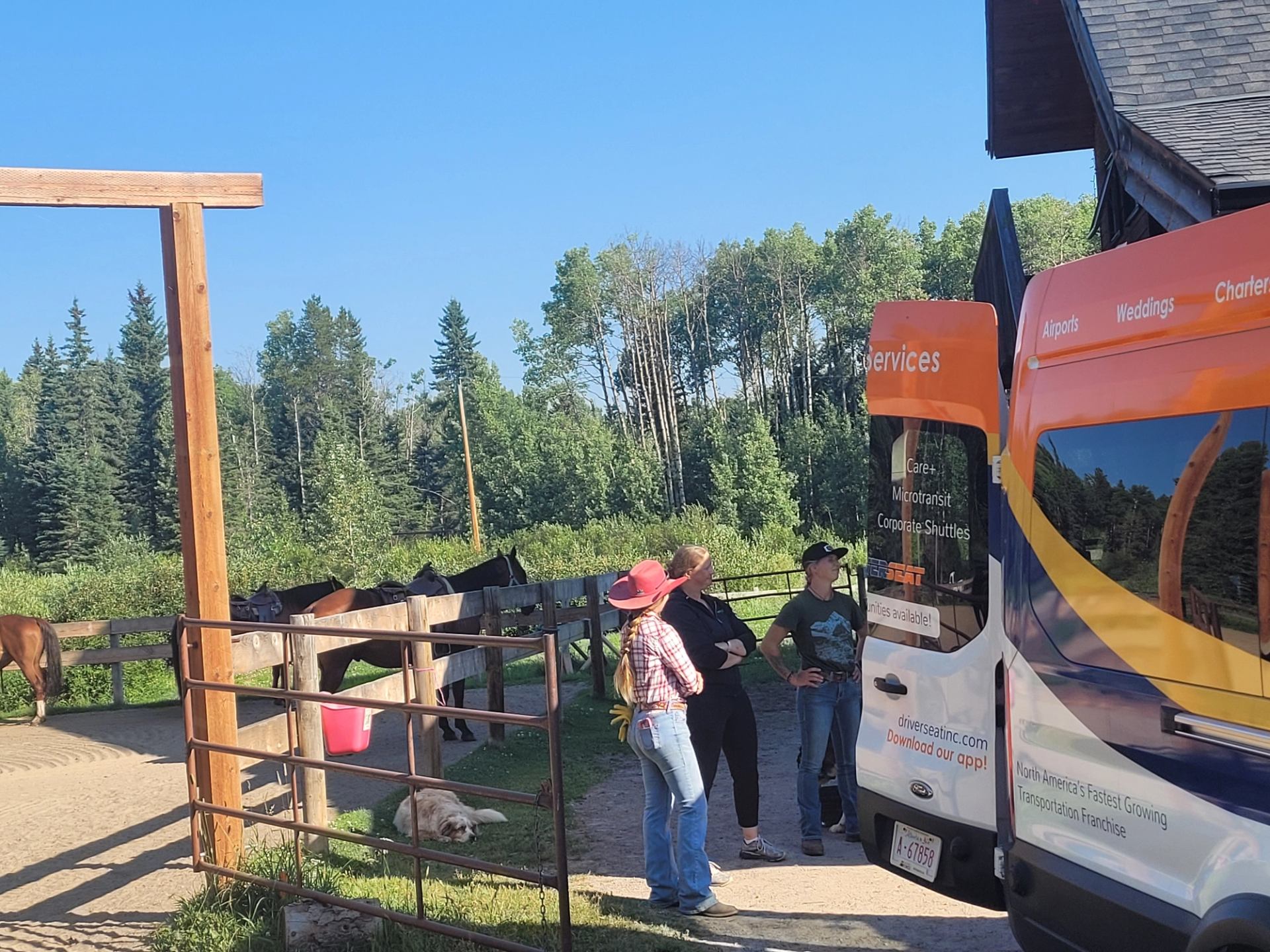 Group of guests standing behind a shuttle van with the door open. Horses in the background.