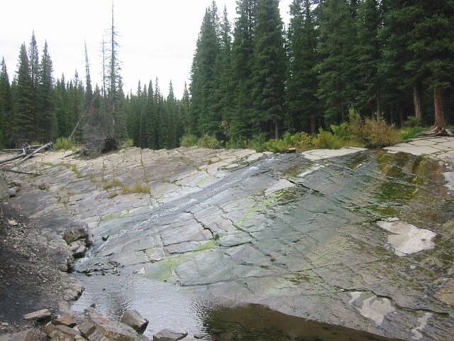 Water flows over smooth rocks in forested landscape.