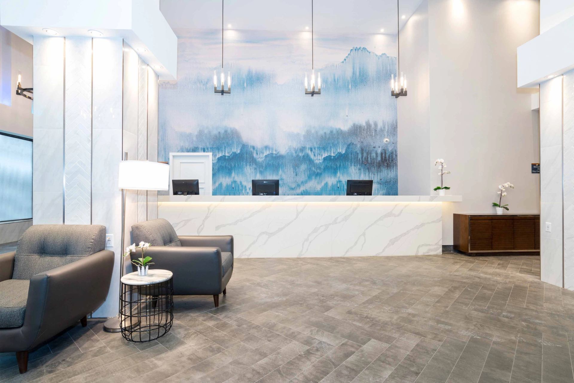 Hotel lobby reception desk with blue mural, lounge chairs and hanging pendant lights.