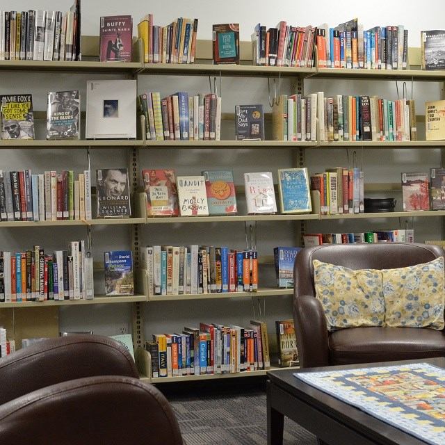 Library bookshelf with novels and chairs beside a small table with a book display.
