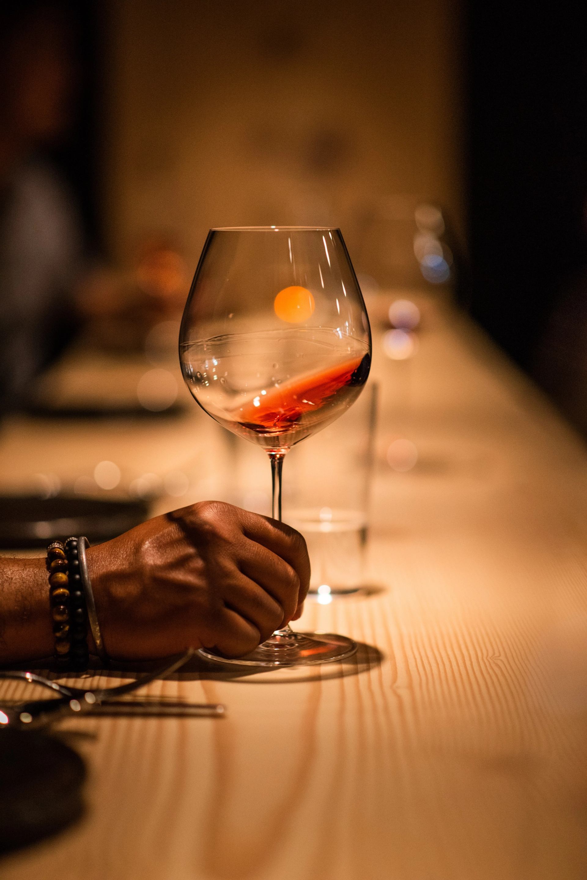 Wine glass with orange garnish held over a wooden counter with warm ambient lighting
