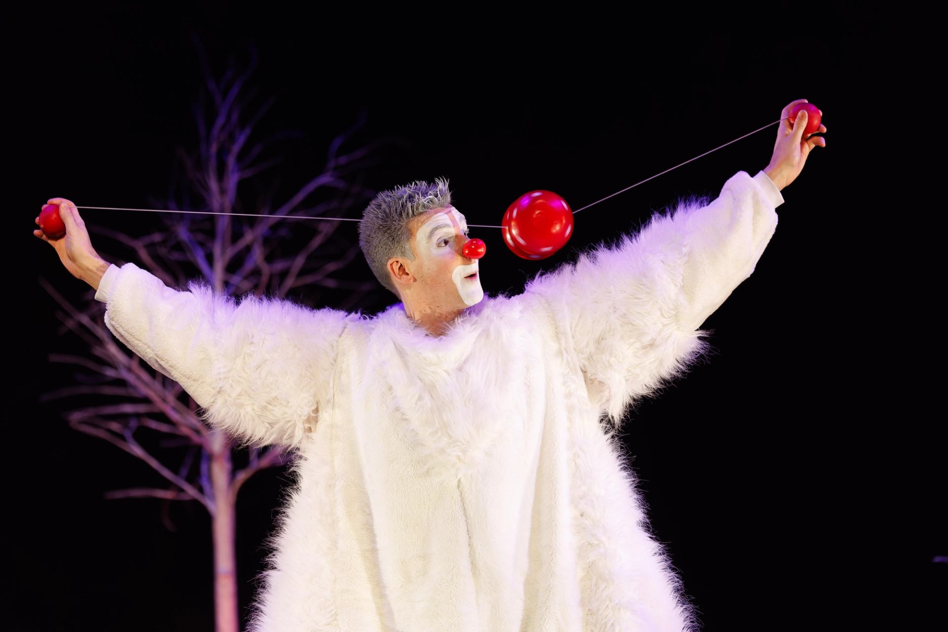 Performer in white furry costume spins red yo-yo near face on dark stage.