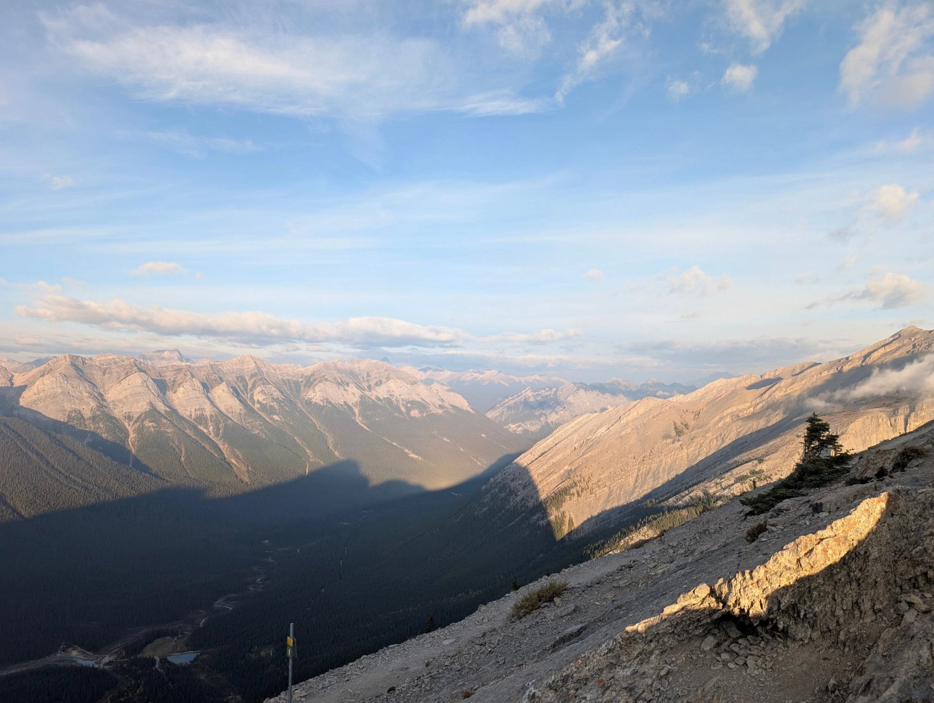 Rocky mountain range with deep valley, long shadows and partly cloudy blue sky.