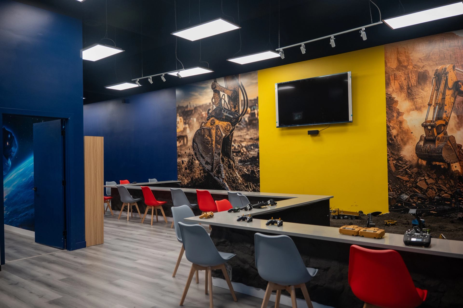 Training room with excavator murals, remote controls, chairs and a wall-mounted screen.