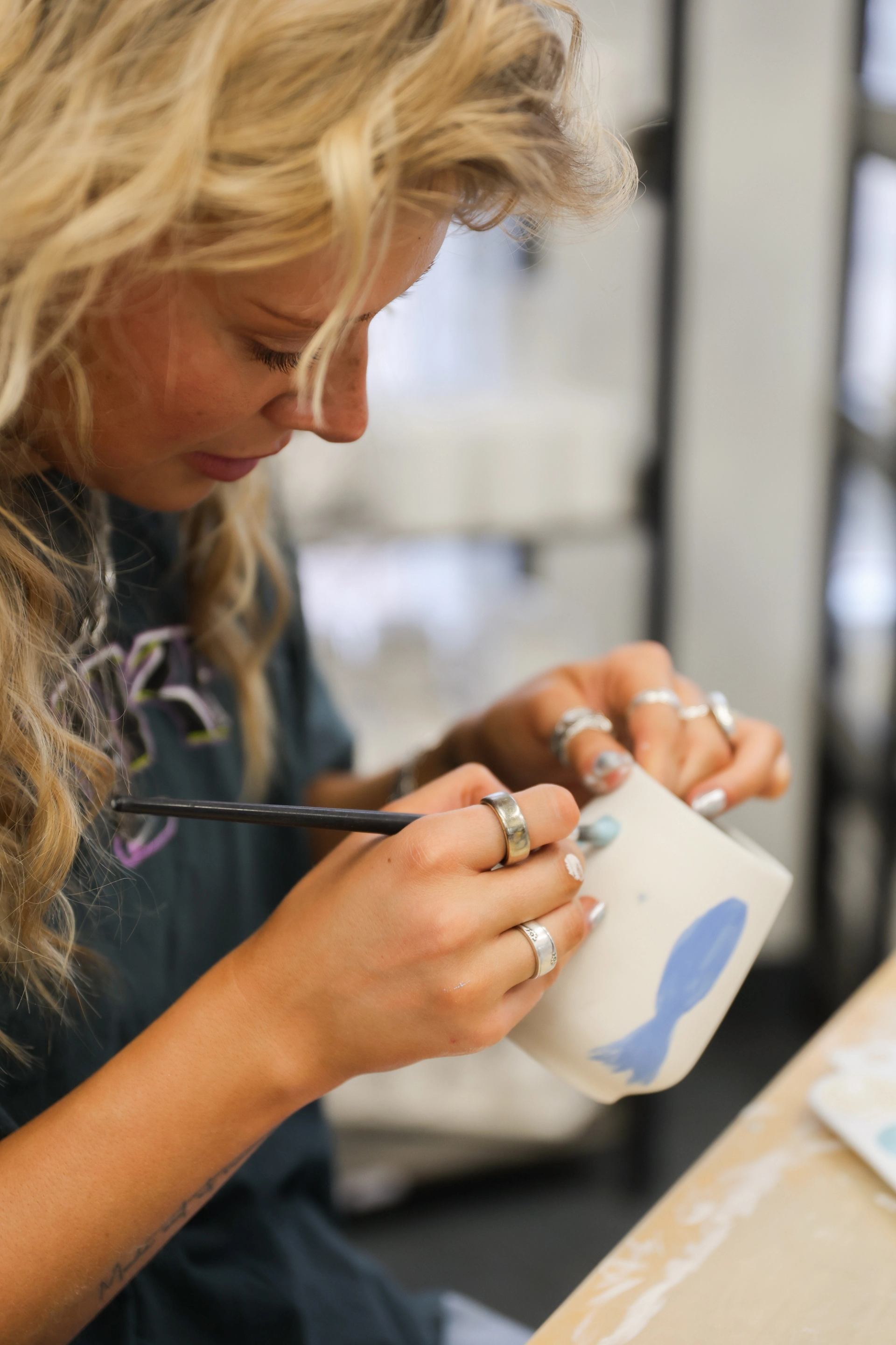 Person painting a ceramic mug with a blue fish design at a table.