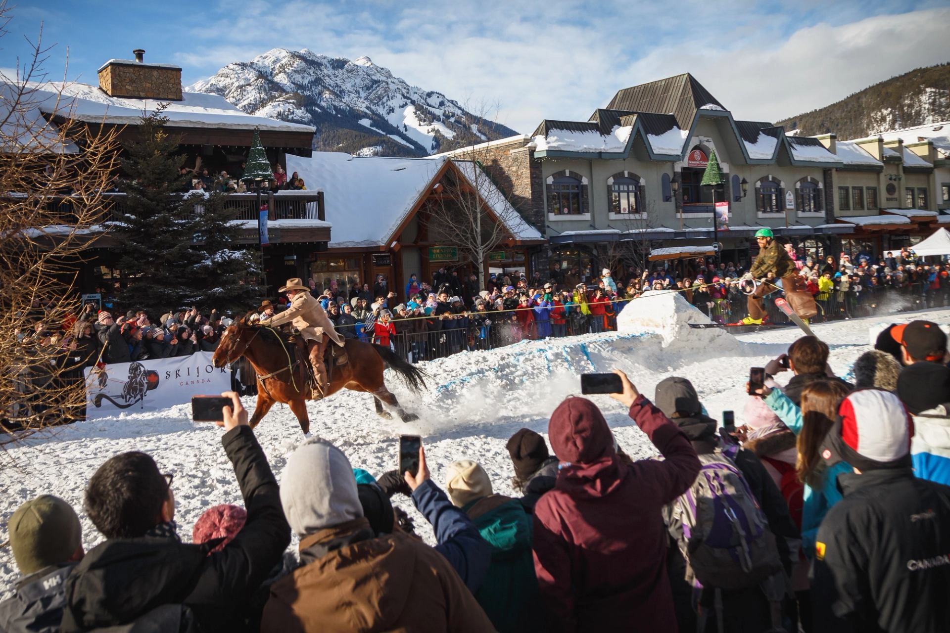 Crowd watches skiers and riders in snowy mountain town.